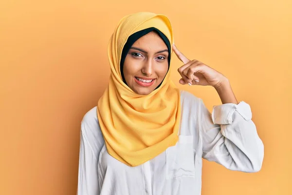 Young brunette arab woman wearing traditional islamic hijab scarf smiling pointing to head with one finger, great idea or thought, good memory