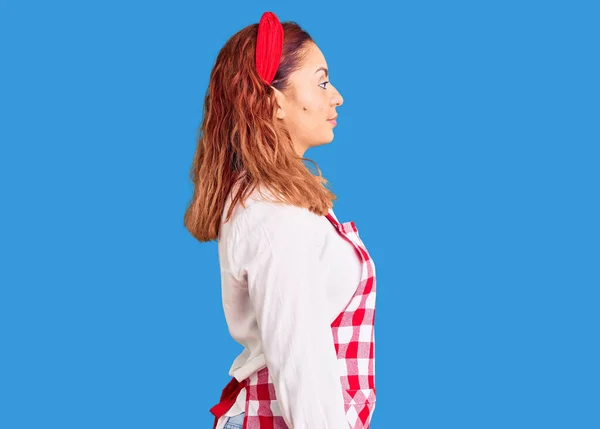 Young latin woman wearing apron looking to side, relax profile pose with natural face with confident smile.