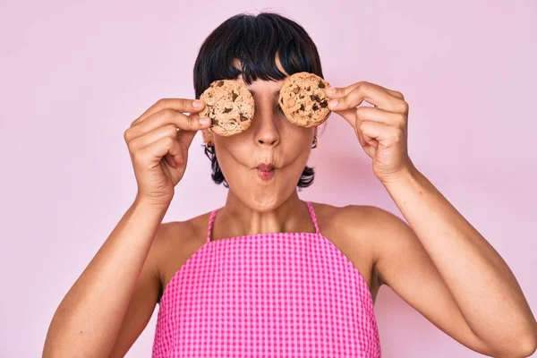 美しいブルネットの女性を保持チョコレートチップクッキー目に魚の顔を作ります口と目を細めて クレイジーでコミカル — ストック写真