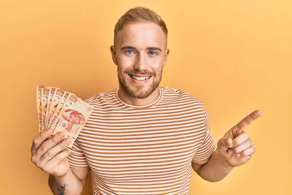 Meksika pezosu tutan genç beyaz adam mutlu bir şekilde gülümsüyor. 