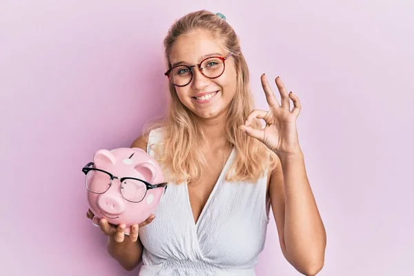 Jong Blond Meisje Holding Piggy Bank Met Bril Doen Teken — Stockfoto