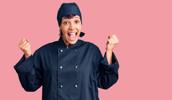 年轻的黑发女子 身穿职业厨师制服 高举双臂 睁大眼睛 为成功感到惊讶和惊奇 获奖者概念 — 图库照片