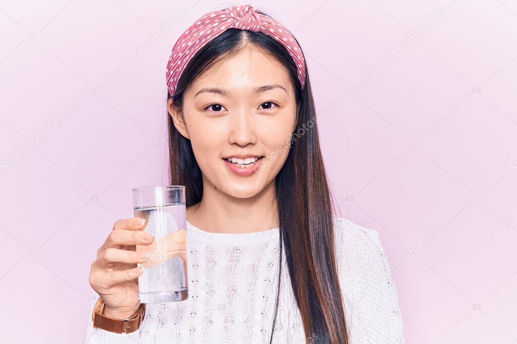 Young beautiful chinese woman drinking glass of water looking positive and happy standing and smiling with a confident smile showing teeth 