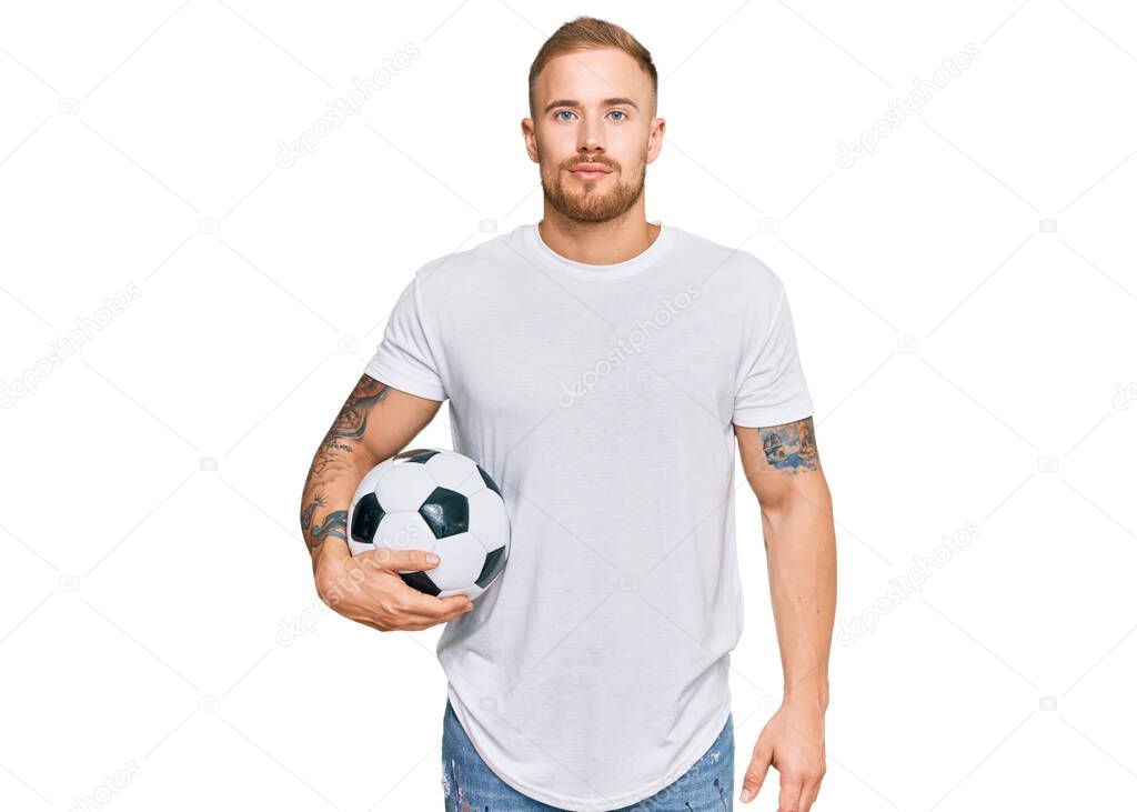 Young irish man holding soccer ball thinking attitude and sober expression looking self confident 