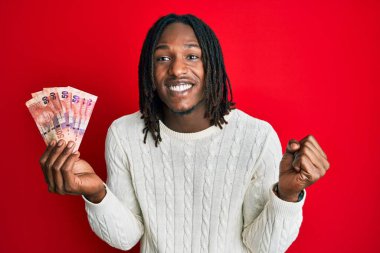 Afrika saçı örülü Afrikalı 50 rand 'lık banknotlar tutan Afrika kökenli Amerikalı adam gururla bağırıyor, zaferi kutluyor ve başarıyı kollarını kaldırarak kutluyor. 