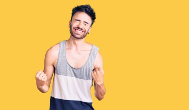 Gündelik kıyafetler giyen genç İspanyol adam çok mutlu ve heyecanlı. Kazanan jestler yapıyor. Kolları havada, gülümsüyor ve başarı için bağırıyor. kutlama konsepti. 
