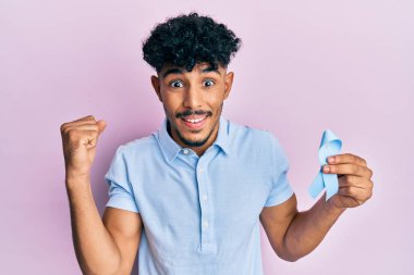 Genç Arap yakışıklı adam mavi kurdele tutuyor gururla bağırıyor, zaferi kutluyor ve başarıyı kollarını kaldırarak kutluyor. 