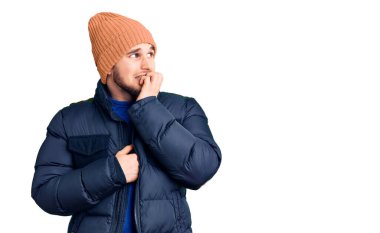 Kışlık giysiler giyen genç yakışıklı adam gergin ve elleri ağızdan tırnak yerken gergin görünüyor. anksiyete. 