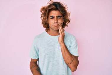 Günlük kıyafetler giyen genç İspanyol adam diş ağrısı ya da diş hastalığından dolayı acı dolu bir ifadeyle ağıza dokunuyor. dişçi 