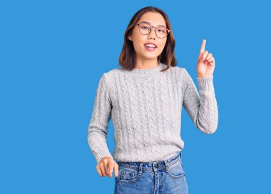 Genç, güzel Çinli kız, günlük kıyafetler giyip bir numaralı parmağını gösterirken, kendinden emin ve mutlu bir şekilde gülümsüyor.. 