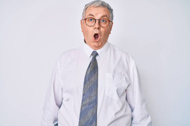 İş kıyafetleri giymiş yaşlı, gri saçlı bir adam ağzı açık kalmış, korkmuş ve şaşkına dönmüş. 