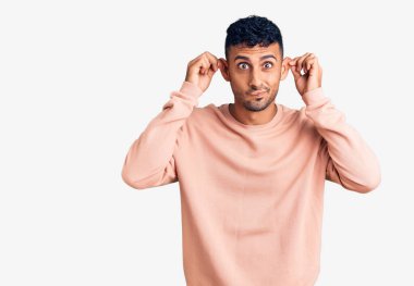 Günlük kıyafetler giyen, gülümseyen, parmaklarıyla kulaklarını çeken genç İspanyol bir adam, komik bir jest. deneme sorunu 