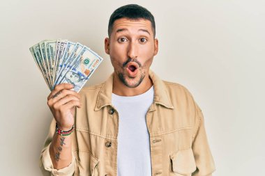 Dövmeleri olan yakışıklı bir adam. Dolarları tutuyor. Korkmuş ve ağzı açık, şaşırmış ve şaşırmış. 