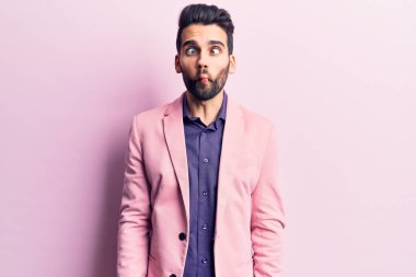 Sakallı, zarif ceketli, dudağıyla balık suratlı, çılgın ve komik bir jest yapan yakışıklı bir genç. Komik ifade. 