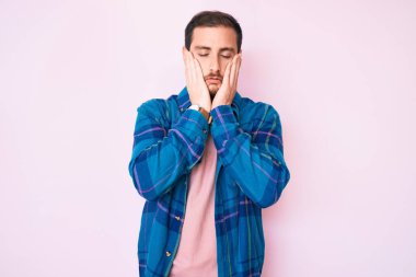 Gündelik kıyafetler giyen genç yakışıklı adam yorgun eller yüzünü kapatıyor, depresyon ve üzüntü, sorun yüzünden üzgün ve sinirli. 