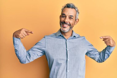 Orta yaşlı, gri saçlı, günlük kıyafetler giyen, kendine güvenen, gülümseyen, kendini gururlu ve mutlu gösteren bir adam.. 