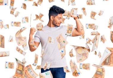 Yakışıklı, Latin Amerikalı, sıradan tişörtler giyen, gururla gülümseyen kol kaslarını gösteren genç adam. fitness konsepti.