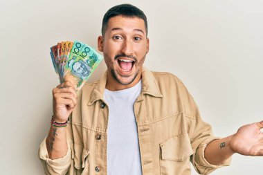 Dövmeleri olan yakışıklı bir adam Avustralya dolarlarını elinde tutuyor başarıyı mutlu bir gülümsemeyle kutluyor ve kazanan el kaldırarak ifade ediyor. 