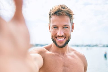 Güneşli bir günde sahilde selfie çeken yakışıklı, beyaz bir adam.