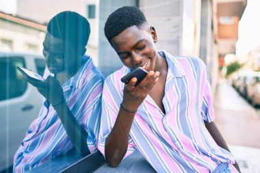 Genç Afrikalı Amerikalı gülümseyen adam şehrin caddesindeki akıllı telefonda mutlu bir şekilde konuşuyor..