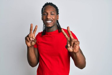 Saçları örgülü Afro-Amerikan bir adam gülümseyerek kameraya bakıyor ve zafer işareti yapıyor. İki numara.. 