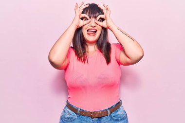 Genç ve cüsseli bir kadın sıradan kıyafetler giyiyor. Dürbün gibi jest yapıyor. Dürbün dilini çıkarıyor, gözler parmaklarından bakıyor. çılgın ifade. 