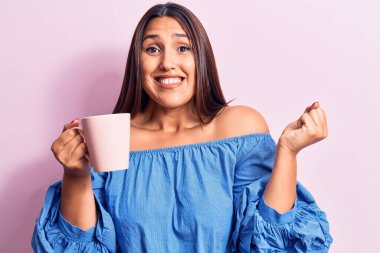 Genç, güzel esmer kadın bir kupa kahve içiyor gururla bağırıyor, zaferi kutluyor ve başarıyı kollarını kaldırarak kutluyor. 