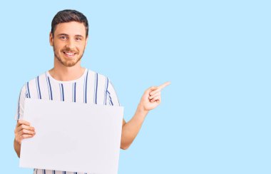 Elinde boş pankart tutan yakışıklı genç adam gülümsüyor mutlu bir şekilde elini ve parmağını yana uzatıyordu. 