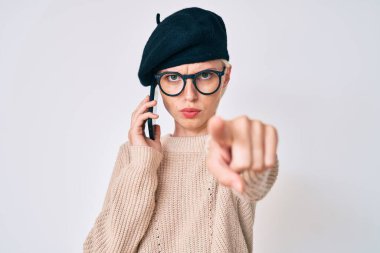 Fransız tarzı giyinen genç beyaz bir kadın akıllı telefondan konuşuyor kamerayı işaret ediyor ve sen kendine güvenen ciddi bir hareket yapıyorsun. 