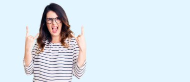 Güzel, genç, esmer bir kadın, günlük kıyafetler ve gözlük takmış, çılgın bir ifadeyle bağırıyor, elleri havada rock sembolü yapıyor. Müzik yıldızı. ağır kavram. 