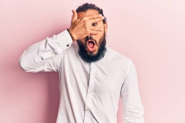 Gündelik kıyafetler giyen genç Arap adam şok içinde yüzünü ve gözlerini kapayarak utanmış ifadesiyle parmaklarının arasından bakıyor.. 