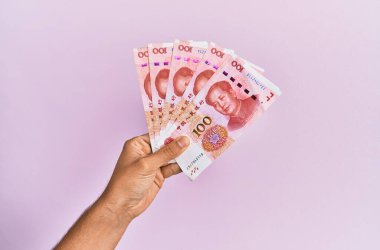 İspanyol eli 100 Yuan 'lık Çin banknotunu soyutlanmış pembe arka planda tutuyor..