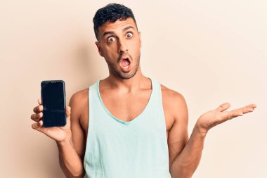 Genç İspanyol asıllı adam elinde akıllı telefonuyla ekranda başarıyı mutlu bir gülümsemeyle ve kazanan yüz ifadesiyle kutluyor. 