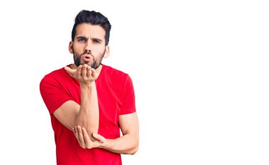 Sakallı, sıradan tişörtlü, kameraya bakıp havada el sallayan, güzel ve seksi genç bir adam. aşk ifadesi. 