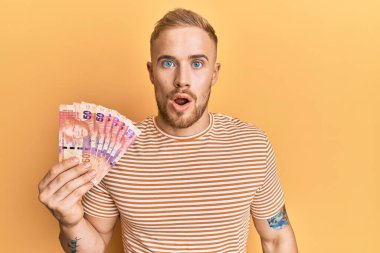 Güney Afrika 'nın 50 rand banknotunu elinde tutan Kafkasyalı genç bir adam korkmuş ve şaşırmış bir şekilde ağzı açık kalmış, inançsız bir yüz. 