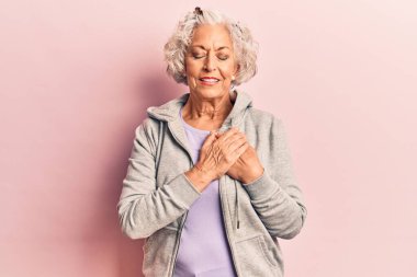 Üstün gri saçlı, sıradan spor kıyafetler giyen, göğsünde elleri kapalı, yüzünde minnet ifadesi olan bir kadın. sağlık kavramı. 