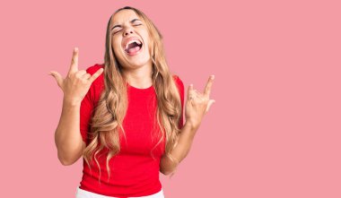 Genç, güzel, sarışın, günlük kıyafetler giymiş çılgın bir ifadeyle bağıran ellerini kaldırarak rock sembolü yapan bir kadın. Müzik yıldızı. ağır kavram. 