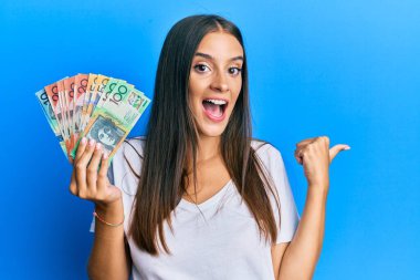 Avustralya doları tutan genç İspanyol kadın başparmağıyla yan tarafa bakıyor, ağzı açık gülümsüyor. 