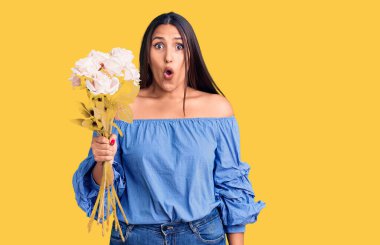Genç, güzel, esmer bir kadın elinde buketi tutuyor. Korkmuş ve ağzı açık kalmış, şaşırmış ve şaşırmış. 