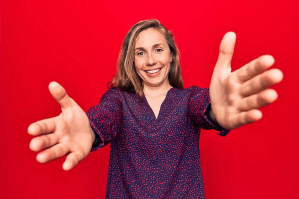 Genç, güzel, sarışın bir kadın, izole edilmiş arka planda dikilip kameraya bakıyor ve sarılmak için kollarını açmış gülümsüyor. Mutluluğu kucaklayan neşeli bir ifade.. 