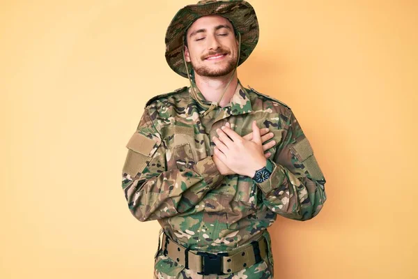 カモフラージュ軍の制服を着た若い白人男性が目を閉じて胸の上で手で笑みを浮かべて 顔に感謝のジェスチャー 健康の概念 — ストック写真
