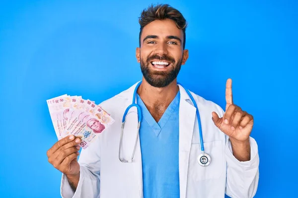 Joven Hispano Vistiendo Uniforme Médico Sosteniendo Pesos Mexicanos Sonriendo Con — Foto de Stock