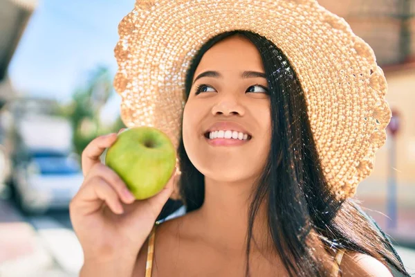 年轻的亚洲女孩笑着在城里吃着一个健康的绿色苹果 — 图库照片