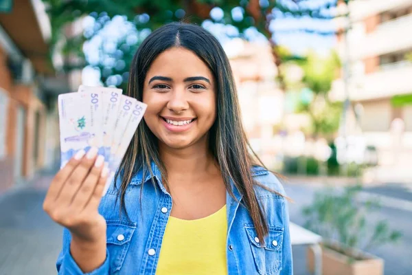 Genç Latin kadın gülümsüyor, elinde Kolombiya pezosu var..