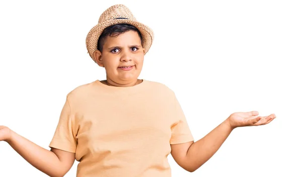 夏の帽子とハワイの水着を身に着けている小さな男の子は 腕や手で混乱した表現を上げました 疑わしい概念 — ストック写真