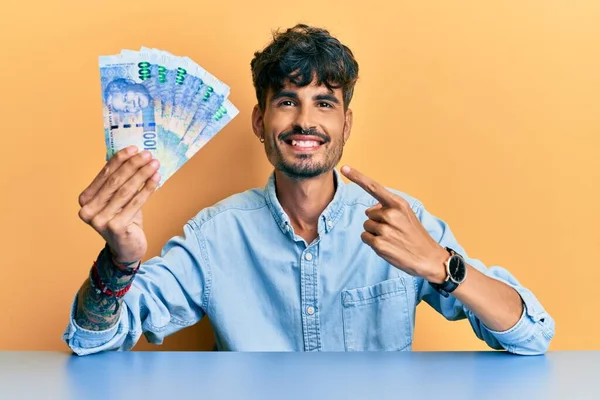 Joven Hispano Sosteniendo Billetes Rand Sudafricanos Sentado Mesa Sonriendo Feliz —  Fotos de Stock