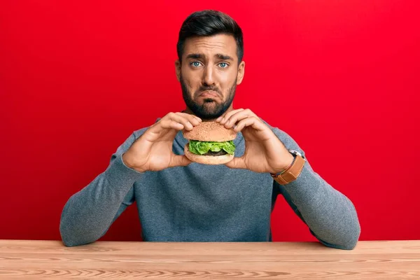 Hombre Hispano Guapo Comiendo Una Sabrosa Hamburguesa Clásica Deprimida Preocupada — Foto de Stock