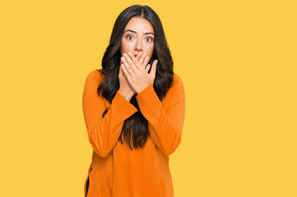 カジュアルなオレンジのセーターを着て美しいブルネットの若い女性は間違いのために手で口をカバーショックを受けた 秘密の概念 — ストック写真