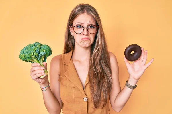 Young Blonde Girl Holding Broccoli Chocolate Donut Depressed Worry Distress — Stock Photo, Image