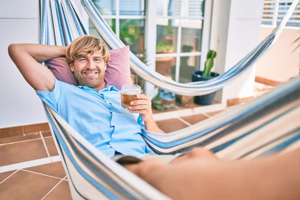 Evinin terasında orta yaşlı yakışıklı bir adam hamakta dinleniyor ve taze bira içiyor.